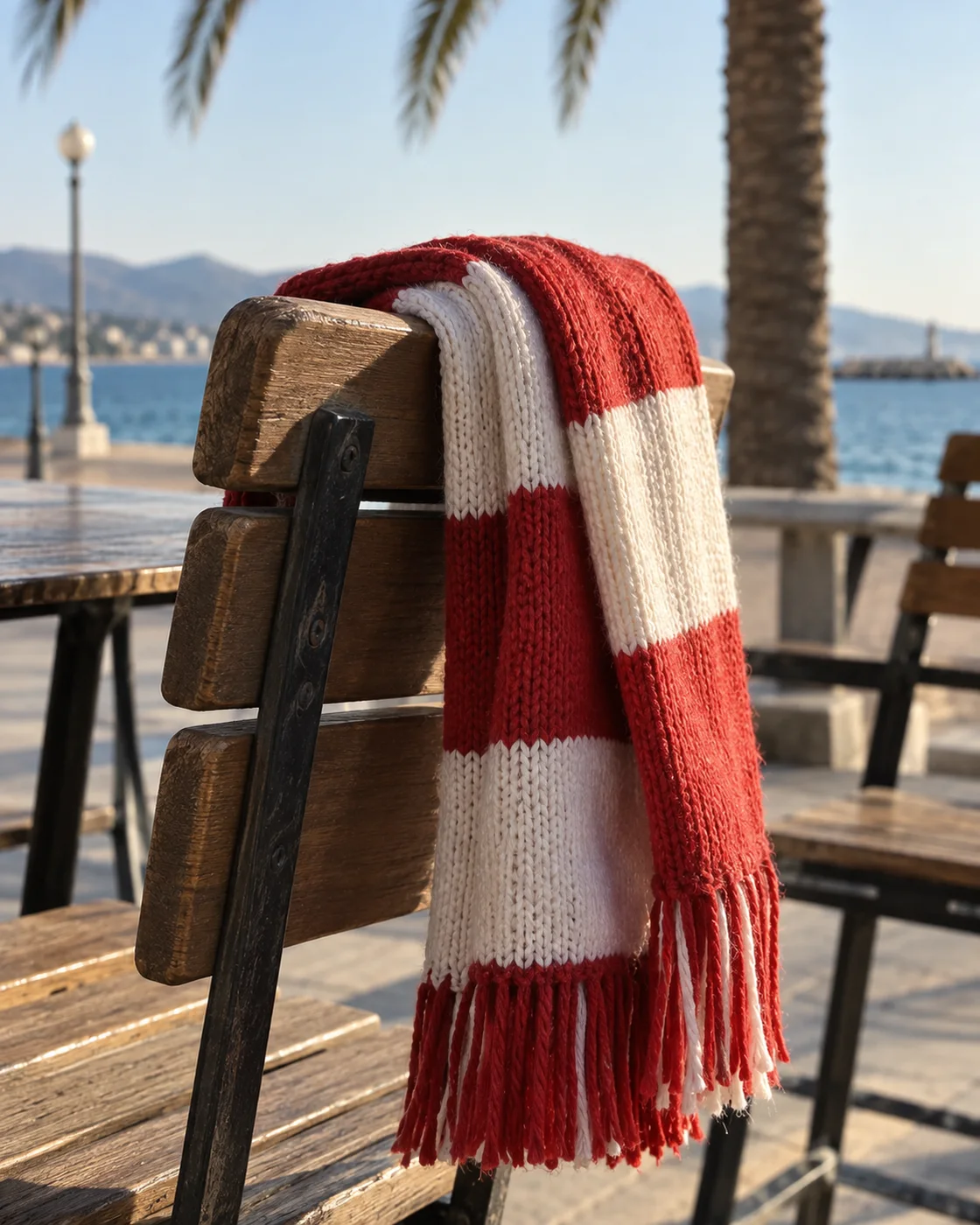 Rot-weisser Strickschal über einer Café-Stuhllehne an einer Strandpromenade